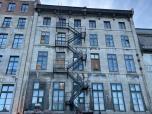 La quatrième image montre un bâtiment ancien, marqué par le temps. Les escaliers de secours en fer forgé, les fenêtres anciennes et les murs usés racontent des histoires de nombreuses générations qui ont habité ces lieux.